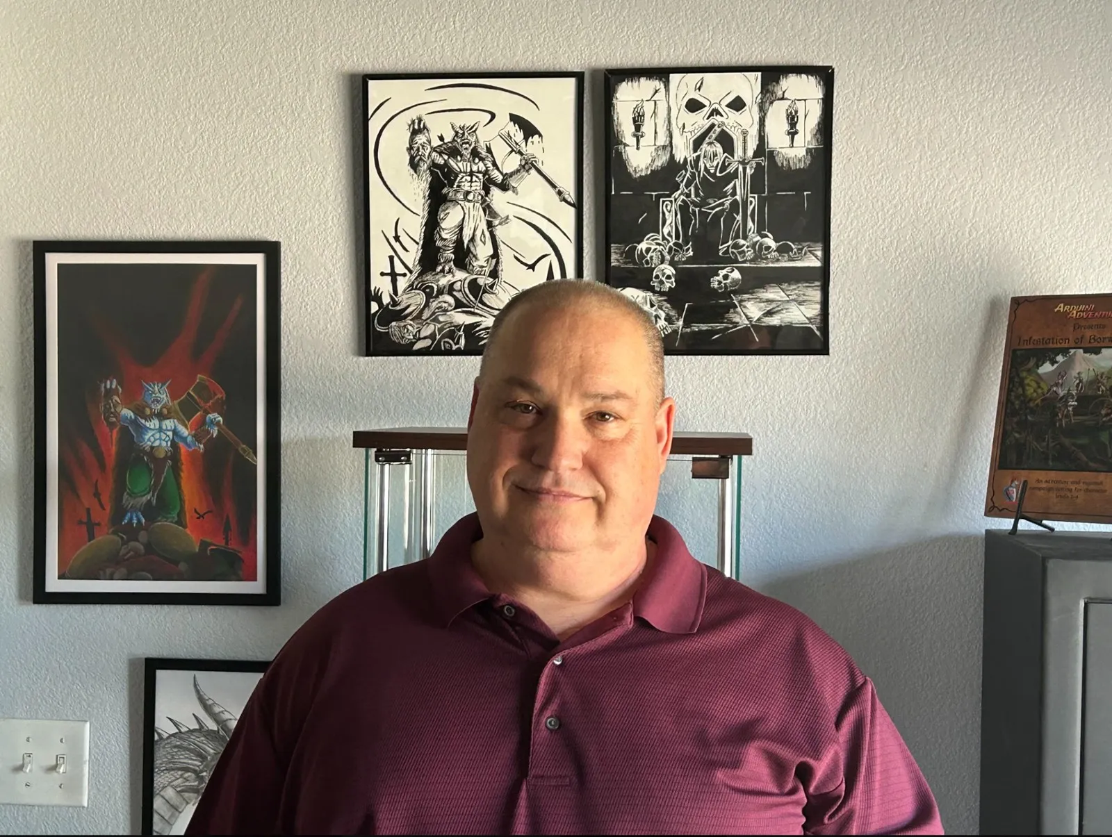 Adrian Arduini in his studio, his framed artwork on the wall behind him.